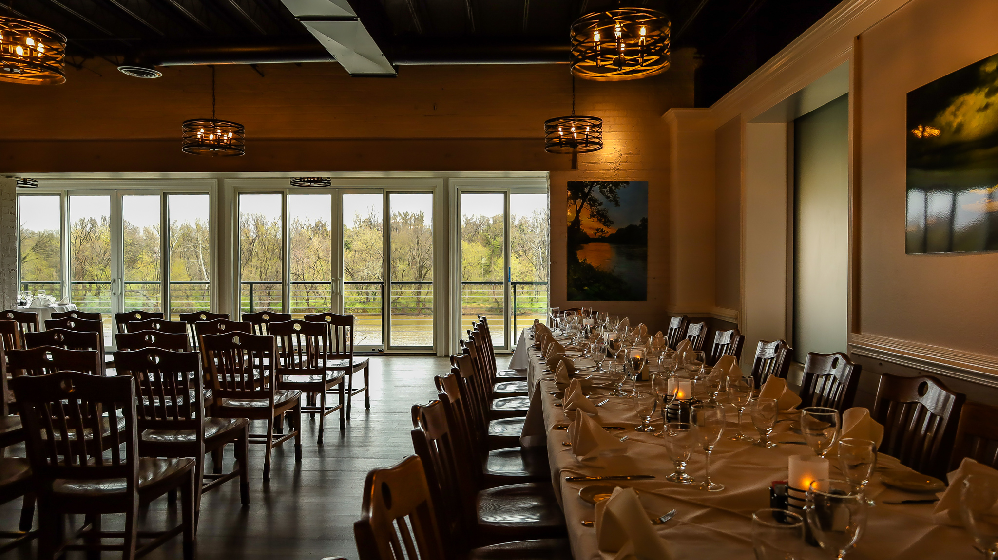 Elegant dining room with a long table set for a formal event and large windows overlooking greenery.