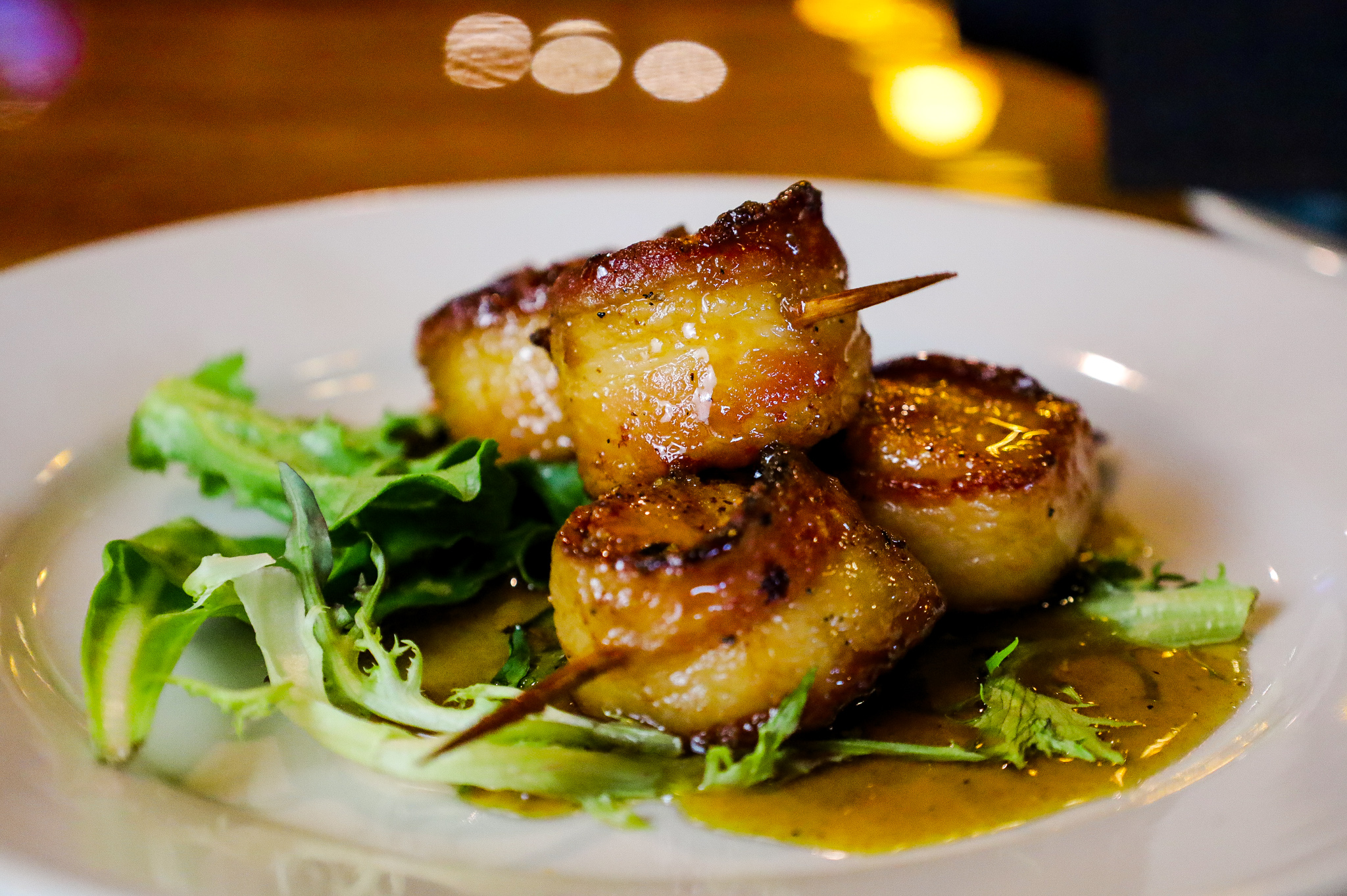 Grilled scallops with a fresh side salad on a wooden plate.