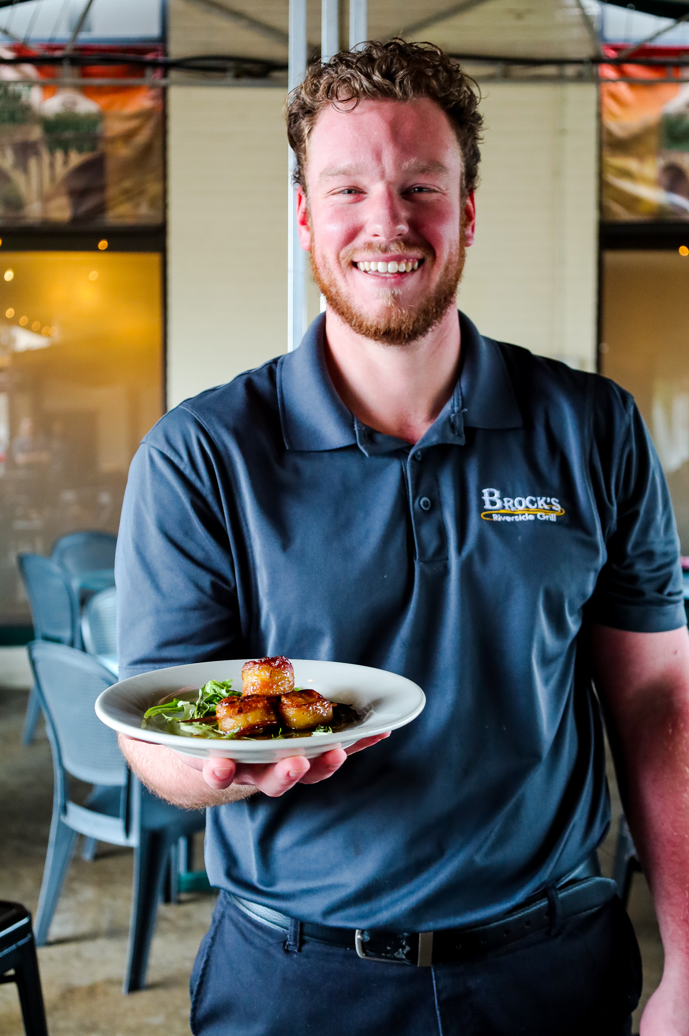 Smiling waiter presenting a plated dish in a restaurant.