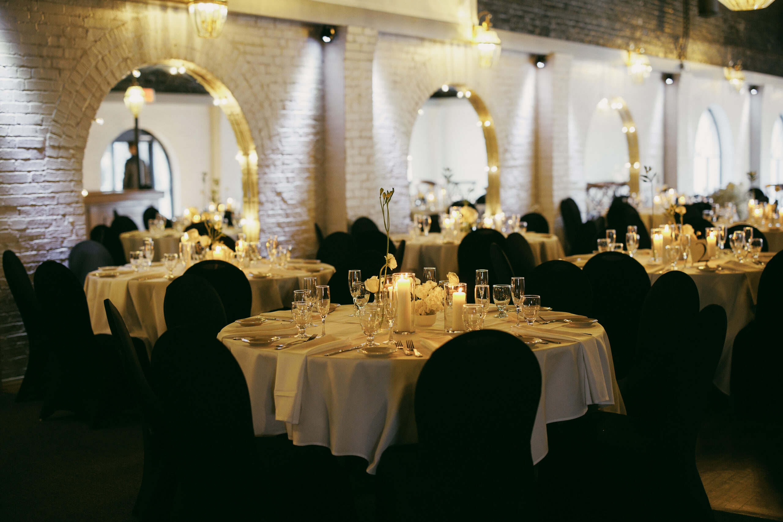 Elegant banquet hall with round tables and black chair covers.